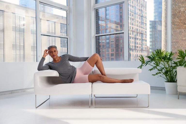 Side view of pink anti-chafe biker shorts showcasing mid-thigh coverage with model reclining on white sofa in sunlit loft