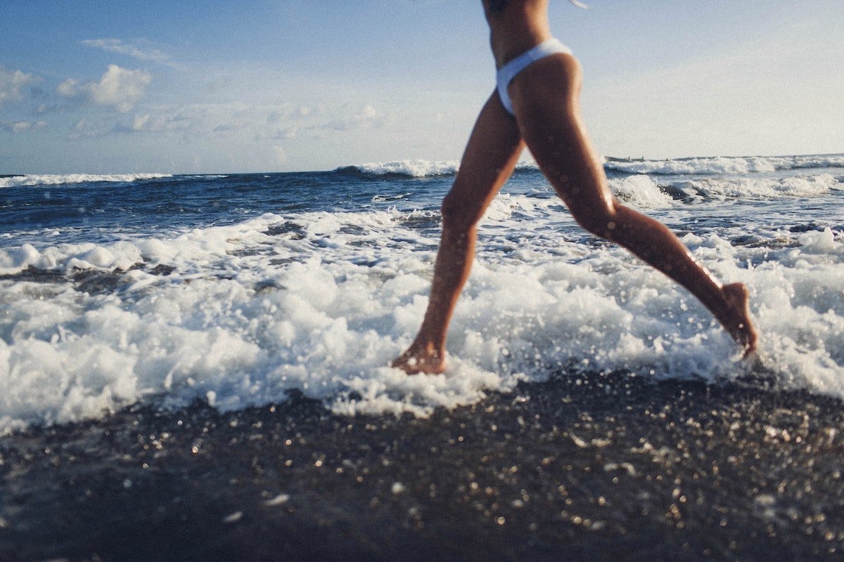 Woman running through shallow ocean waves wearing white bikini bottoms on a sunny beach