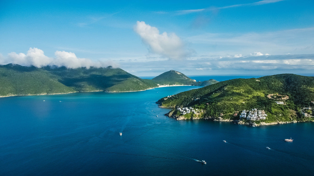 Aerial view of green islands and a turquoise bay with small boats on calm blue water under a partly cloudy sky