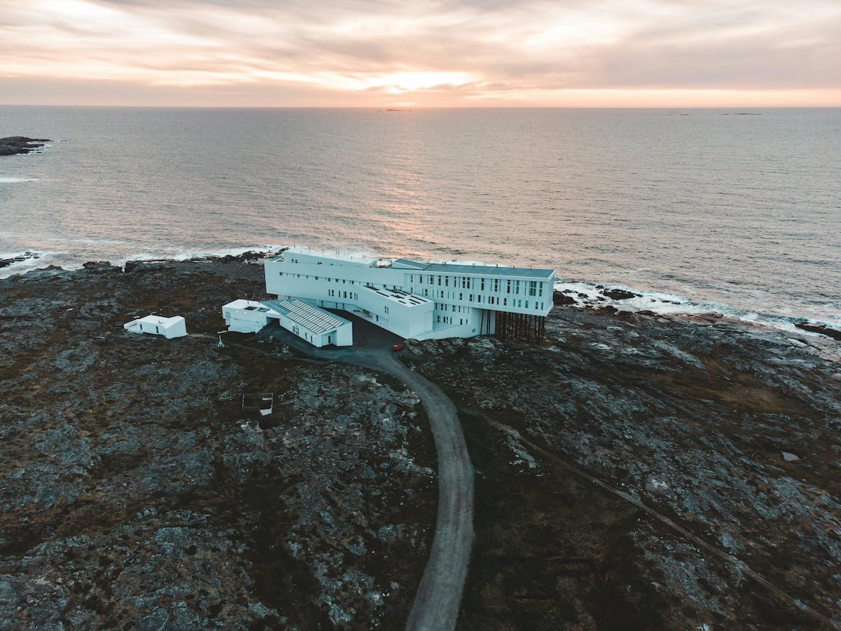 Aerial view of a modern white seaside hotel on a rocky coast at sunset