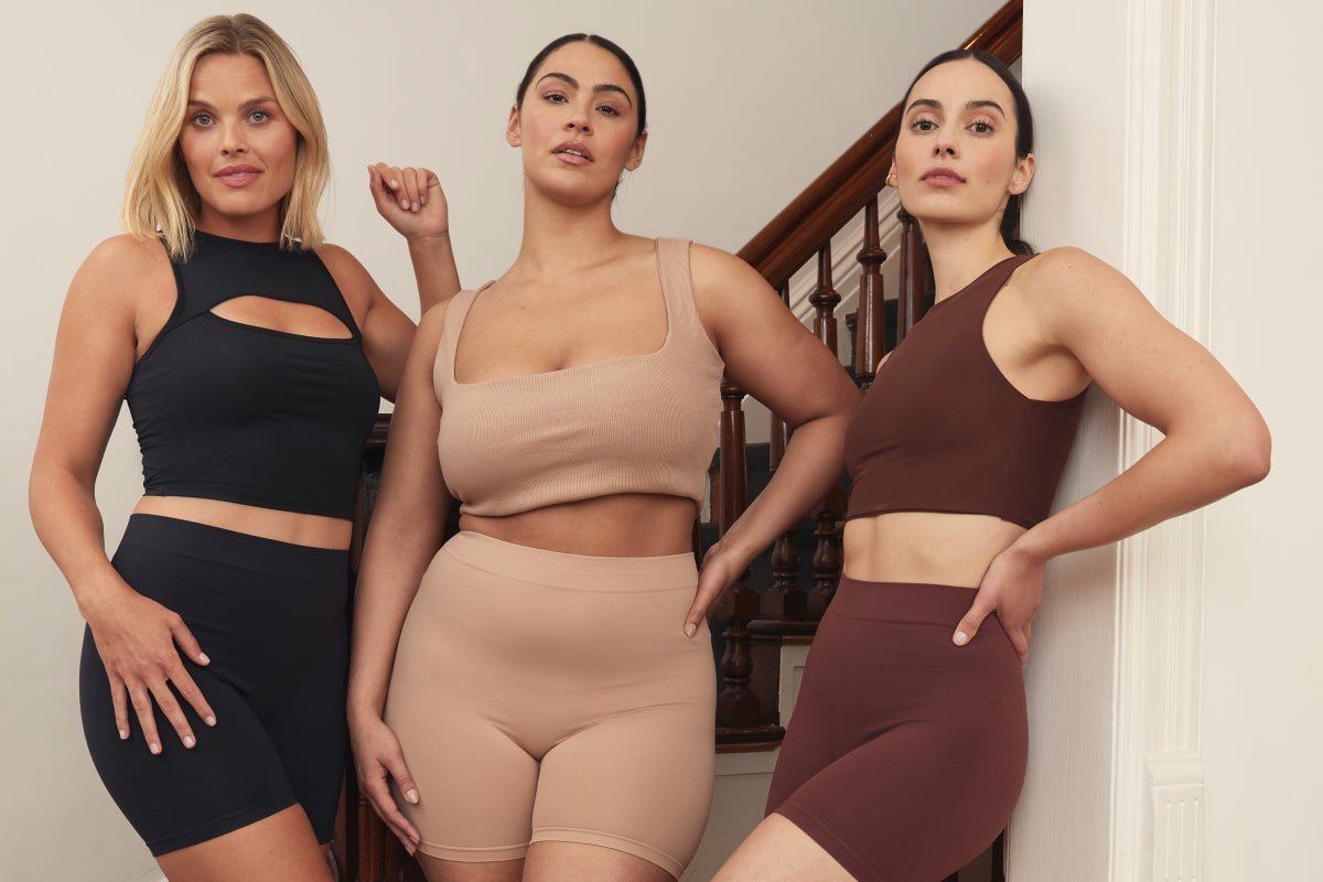 Front view of three models wearing Thigh Society shorties showing smooth mid-thigh fit in black, nude, and brown on stairs