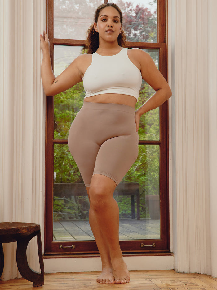 Front view of Original 9 inch taupe anti-chafe shorts showing high waist and mid-thigh fit on model in front of window with garden outside