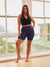 Front of The Staple maternity 7-inch indigo shorts on model showing high-rise waistband and mid-thigh length in sunlit window